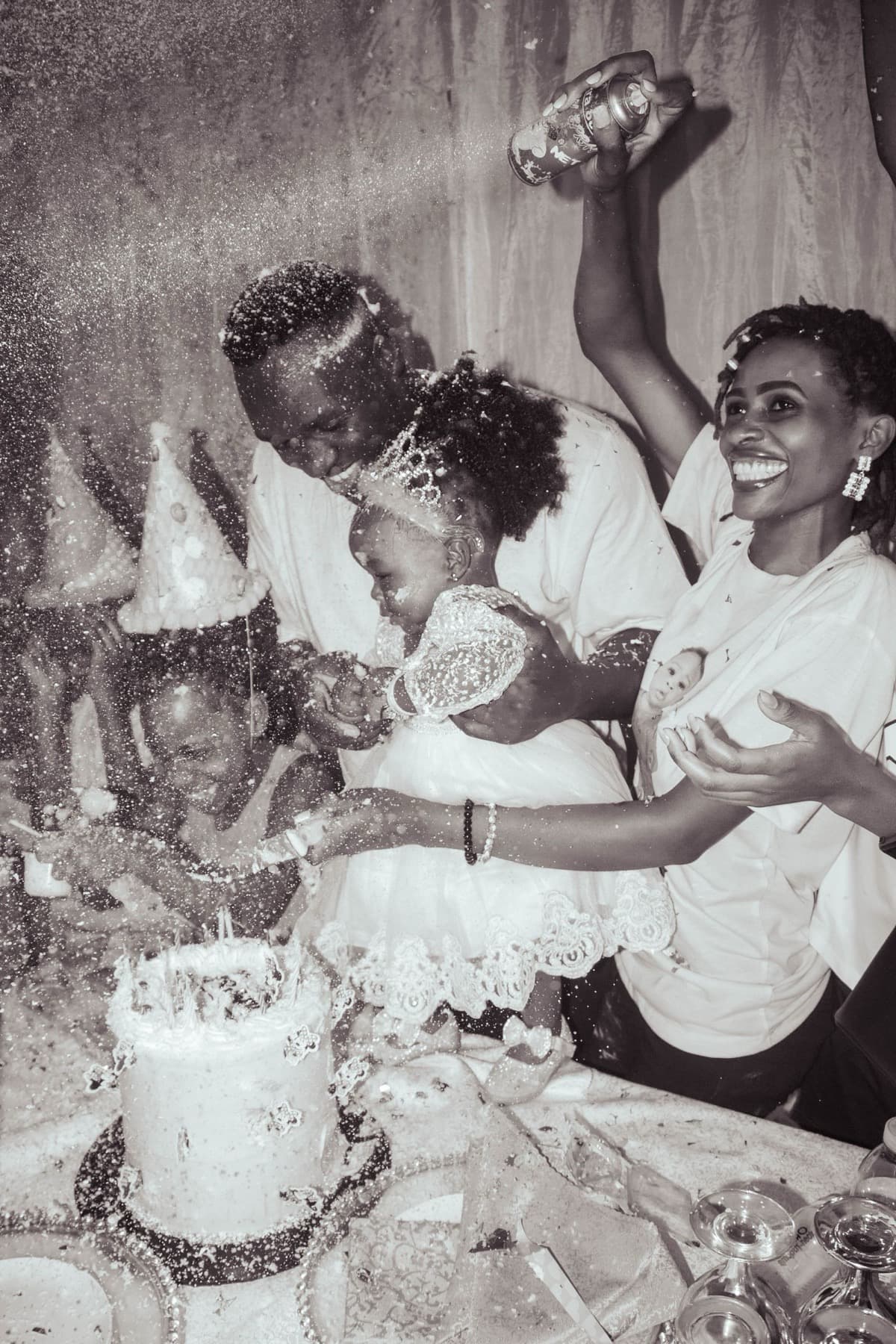 Una famiglia taglia la torta di compleanno in bianco e nero, cappellini in testa