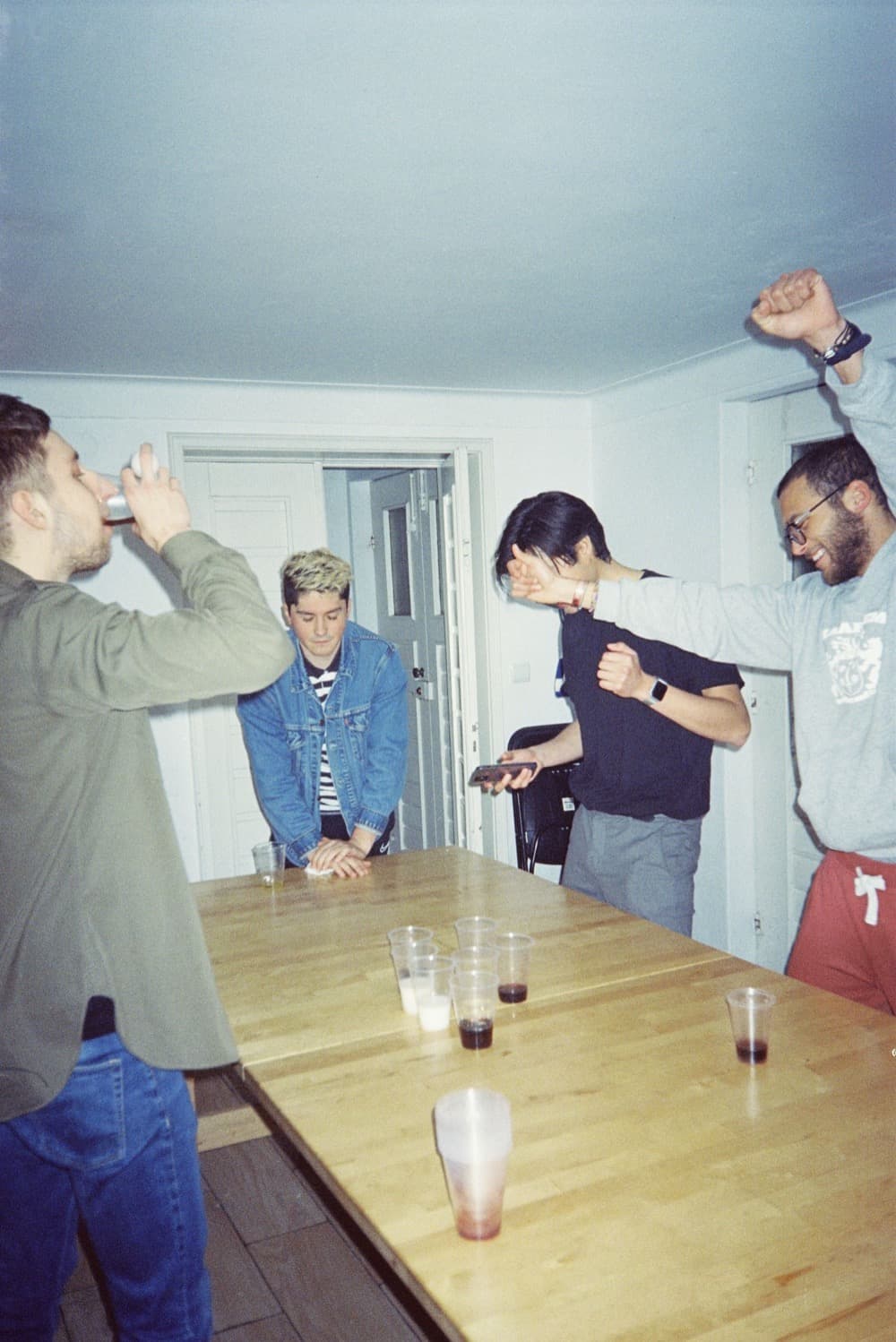 Friends playing beer pong in a bare kitchen under direct flash
