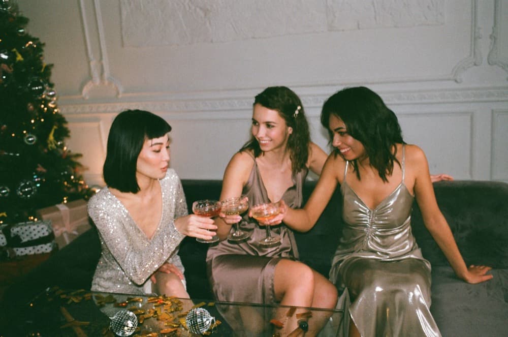 Three friends in sequins sharing drinks on a sofa